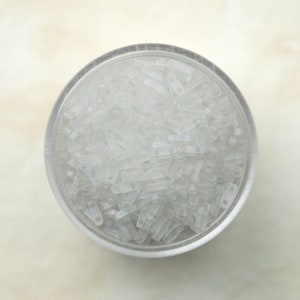 May include: A clear plastic container filled with small, white, opaque, rectangular beads.