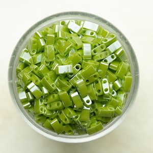 May include: A glass bowl filled with green glass seed beads. The beads are small and rectangular with two holes in each.