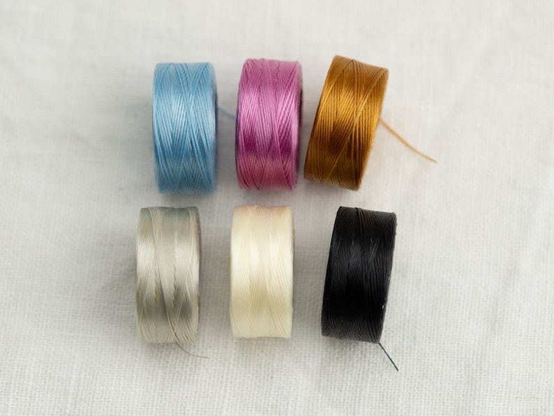 Peut inclure: Six bobines de fil de diff&eacute;rentes couleurs, notamment bleu clair, rose, or, gris clair, blanc et noir.