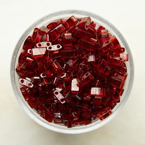 May include: A clear glass bowl filled with small, dark red, rectangular glass beads.