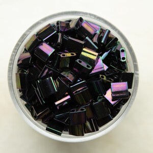 May include: A bowl filled with iridescent black square beads. The beads have a subtle rainbow sheen.