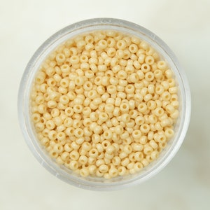 May include: A clear plastic container filled with small, cream-colored beads.
