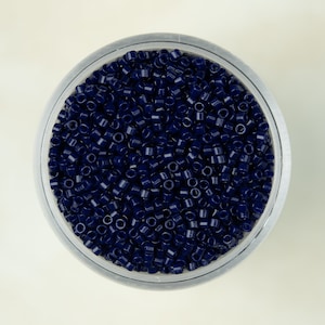 May include: A close-up view of a clear container filled with dark blue seed beads.