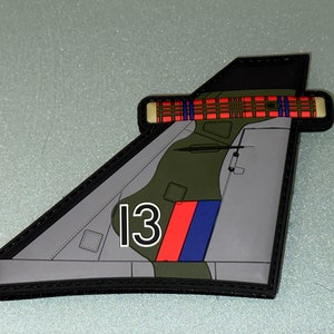 May include: A grey, green and red embroidered patch shaped like a plane's tail fin. The patch has a black border and the number "13" in white on the side.