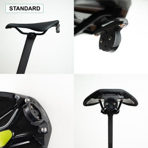 May include: A black bicycle saddle mounted on a seat post, featuring a standard integrated circular mounting bracket attached to the rear rails. The assembly includes metal hardware and a black plastic base, with the text STANDARD visible in the corner.