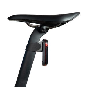 Könnte beinhalten: Ein schwarzer Fahrradsattel auf einer Sattelstütze mit einem vertikalen roten LED-Sicherheitslicht, das an der Stütze befestigt ist. Der Sattel hat eine glatte, konturierte Oberfläche und das Licht ist in einem schwarzen Rahmen mit roter Linse.
