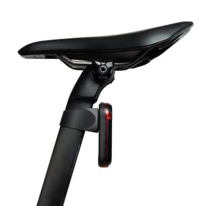 Könnte beinhalten: Ein schwarzer Fahrradsattel auf einer Sattelstütze mit einem vertikalen, schwarz-roten Rücklicht, das an der Stütze befestigt ist. Der Sattel hat eine glatte, konturierte Oberfläche und ist über eine Metallschienenklemme mit der Stütze verbunden.