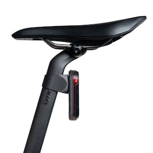 以下が含まれることがあります： マットブラックのシートポストに取り付けられた黒い自転車用サドル。側面にはsyncrosの文字が印字されています。サドルレールのすぐ下に、長方形の赤いLEDセーフティライトがシートポストの後部に取り付けられています。