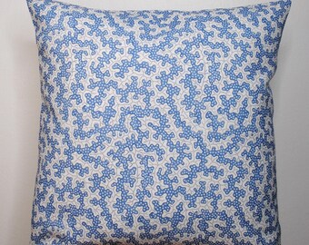 Op de afbeelding: Vierkant decoratief kussen met een blauw en wit koraalpatroon. Het stoffen kussen ligt op een houten oppervlak. Het patroon bestaat uit herhaalde blauwe, koraalachtige vormen tegen een witte achtergrond.