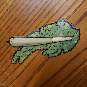 May include: A green and white cartoon illustration of a joint with smoke coming out of it.