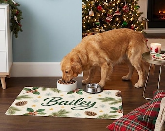 May include: A rectangular pet feeding mat featuring a cream background with a pattern of green pine branches, holly leaves, brown pinecones, and small yellow stars. The name Bailey is printed in large, dark green cursive script in the center.