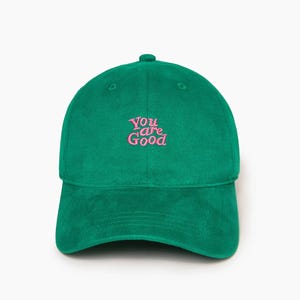 Pode incluir: Boné de beisebol verde com o texto bordado "You are Good" em rosa. O boné tem uma aba curva e um botão na parte superior. O chapéu é feito de um tecido macio.