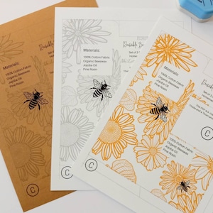 Peut inclure: Trois modèles imprimables pour réaliser des emballages alimentaires réutilisables en cire d'abeille. Les modèles présentent un motif de tournesol et d'abeille en gris, jaune et orange. Le texte sur les modèles indique "Cire d'abeille réutilisable" et "Matériaux : 100 % coton, cire d'abeille biologique, huile de jojoba, colophane".