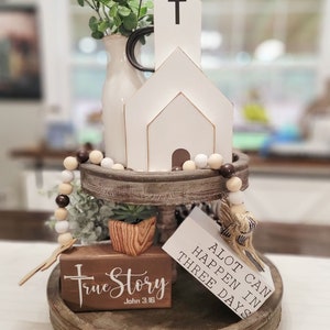 Op de afbeelding: Een houten dienblad met meerdere lagen met een witte houten kerk, een vetplant in een houten pot, een bruine en witte kralenkrans en twee houten borden. De borden tonen "Alot can happen in three days" en "True Story John 3:16".