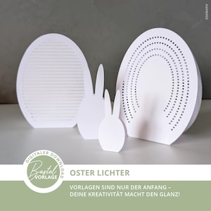 Op de afbeelding: Witte papieren paasdecoraties, waaronder twee eivormen en twee konijnensilhouetten. Eén ei heeft horizontale lijnen, de andere een stippenpatroon. De tekst "OSTER LICHTER" is zichtbaar, samen met andere Duitse tekst.