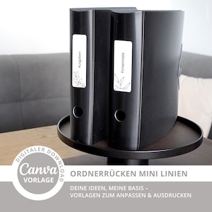 Könnte beinhalten: Schwarze Ordner mit weißen Etiketten mit der Aufschrift "Ausgaben" und "Firmenmiete". Die Ordner stehen auf einem schwarzen Tablett. Das Bild enthält auch den Text "DIGITALER DOWNLOAD Canva VORLAGE ORDNERRÜCKEN MINI LINIEN DEINE IDEEN, MEINE BASIS - VORLAGEN ZUM ANPASSEN & AUSDRUCKEN."