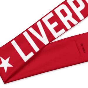 May include: Red headband with the word "LIVERPOOL" in large white letters. A white star is on the left side. The ID number #654 is printed on the right side. The headband is angled diagonally.