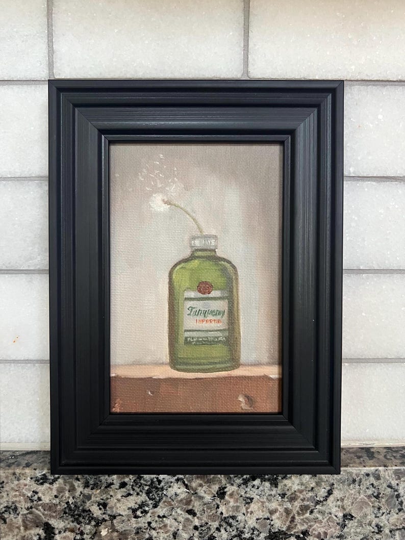 May include: A framed painting featuring a green gin bottle with the Tanqueray label and a single white flower. The artwork is set against a neutral background and framed in a black, rectangular frame.