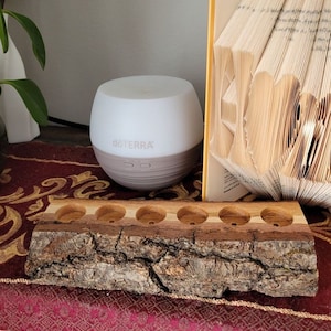 May include: A wooden log with six holes for essential oil bottles. The log is sitting on a red and gold patterned table runner. A white diffuser with the word "dōTERRA" on it is in the background.