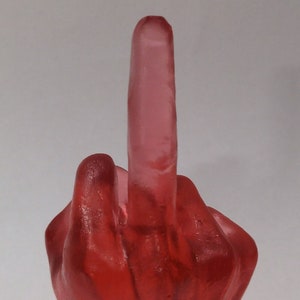 May include: A red glass hand sculpture with the middle finger extended in a rude gesture.