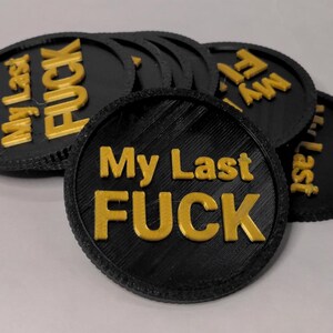 May include: Black and gold round tokens with the text "My Last FUCK" in gold lettering. The tokens are stacked and slightly overlapping, with a textured edge.