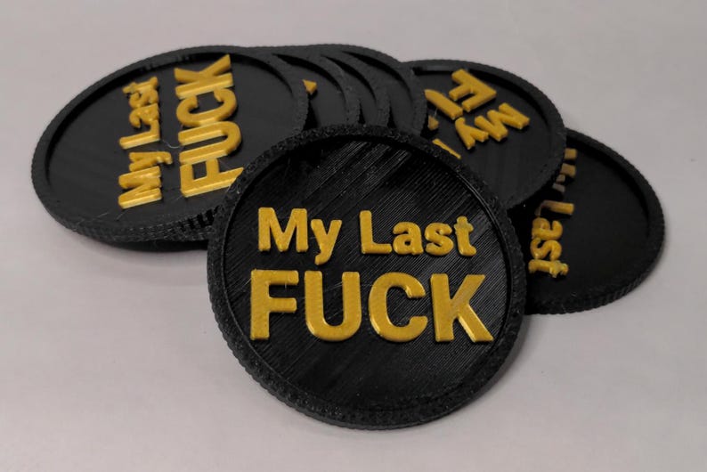 May include: Black and gold round tokens with the text "My Last FUCK" in gold lettering. The tokens are stacked and slightly overlapping, with a textured edge.