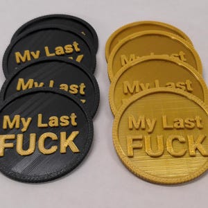 May include: A collection of black and gold round tokens. Each token has the phrase "My Last FUCK" in gold lettering. The tokens are arranged in two groups, one black and one gold.