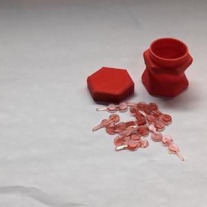 May include: A red hexagonal container with a lid and a red cylindrical container with a lid. Both containers are open and there are many small, clear, plastic, red-tinted,  objects inside the containers.