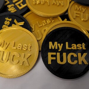 May include: A collection of round tokens in gold and black, each embossed with the phrase "My Last FUCK" in bold, sans-serif letters. The tokens have a textured surface and a ridged edge.