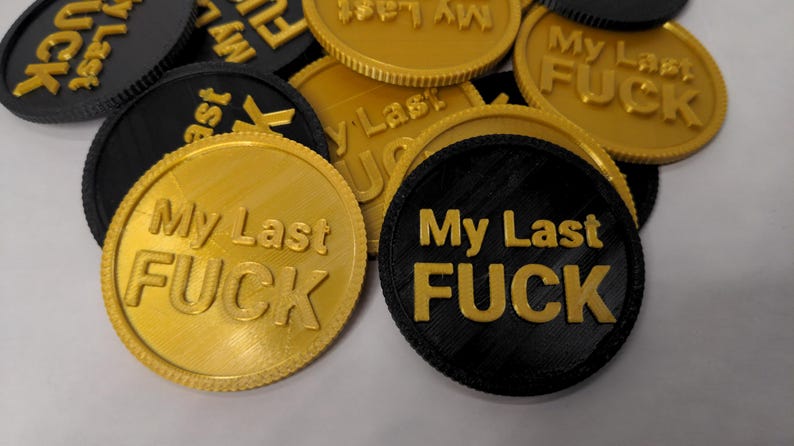 May include: A collection of round tokens in gold and black, each embossed with the phrase "My Last FUCK" in bold, sans-serif letters. The tokens have a textured surface and a ridged edge.