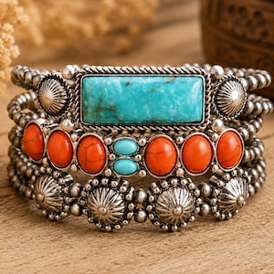 May include: A multi-strand cuff bracelet featuring a central rectangular turquoise stone, flanked by silver sunburst accents. The design includes rows of silver beads, orange oval stones, and two small turquoise ovals set in a silver metal frame.