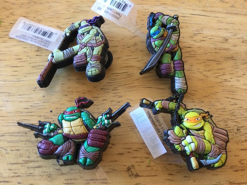 May include: Four Teenage Mutant Ninja Turtles figurines. Each figurine is made of green plastic and features a different turtle with their signature weapon. The turtles are Donatello, Raphael, Leonardo, and Michelangelo.
