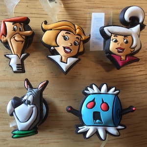 May include: Set of six cartoon character shoe charms featuring characters from the animated television series The Jetsons. The charms are made of rubber and feature George Jetson, Jane Jetson, Elroy Jetson, Astro, Judy Jetson, and Rosie the Robot.