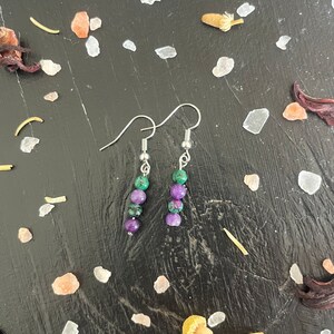 May include: A pair of silver earrings with green and purple gemstone beads. The earrings are dangling and have a simple design.