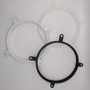 May include: Three circular frames in white, clear, and black. Each frame has four evenly spaced tabs extending outwards. The frames are made of a smooth material, possibly plastic, and are arranged on a white background.
