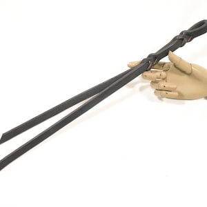 Puede incluir: Una cuerda de plomo de cuero negro con un nudo trenzado en un extremo.