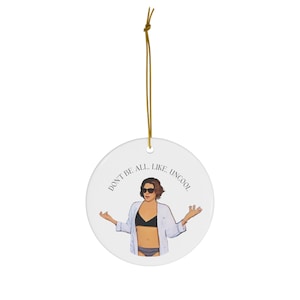 Puede incluir: Un adorno de cerámica blanca con una imagen de dibujos animados de una mujer con gafas de sol y una camisa blanca sobre un bikini. El texto "Don't be all... like, uncool" está impreso alrededor de la imagen.