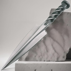 May include: A handcrafted, silver-toned dagger with a twisted handle and a sharp, pointed blade. The dagger is displayed against a textured, gray concrete block, showcasing its intricate design and craftsmanship. The overall aesthetic is minimalist and industrial.