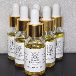 Puede incluir: Seis botellas de vidrio llenas de líquido amarillo. Cada botella tiene una etiqueta blanca con el texto "Pangea's Botanica Clear The Way Oil". Las botellas tienen cuentagotas blancos y collares dorados.