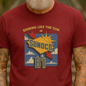 May include: A maroon t-shirt featuring a vintage-style graphic. The design includes the text "SHINING LIKE THE SUN" above a stylized sun and the word "SUNOCO" in a yellow and blue design, with the number "81" below.