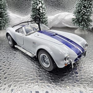 K&ouml;nnte beinhalten: Ein wei&szlig;es und blaues Spielzeugauto mit einem blauen Streifen &uuml;ber der Motorhaube. Das Auto ist eine Nachbildung eines klassischen Sportwagens.