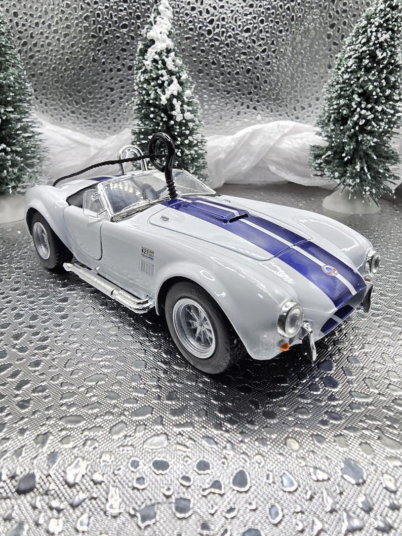 K&ouml;nnte beinhalten: Ein wei&szlig;es und blaues Spielzeugauto mit einem blauen Streifen &uuml;ber der Motorhaube. Das Auto ist eine Nachbildung eines klassischen Sportwagens.