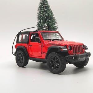 May include: A red Jeep Wrangler Rubicon ornament with black wheels and a black roof. The miniature SUV is detailed with a front grill, headlights, and the word "Rubicon" on the hood. A black string is attached for hanging.