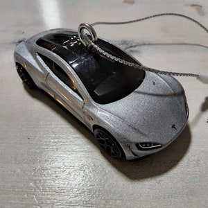 May include: A silver Tesla Model S Plaid toy car ornament with a black interior and a black string for hanging.