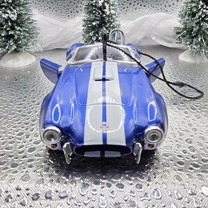 K&ouml;nnte beinhalten: Blau-wei&szlig;es Modellfahrzeug-Ornament mit einem wei&szlig;en Streifen in der Mitte der Motorhaube. Das Auto hat ein schwarzes Band, das an der Oberseite befestigt ist.