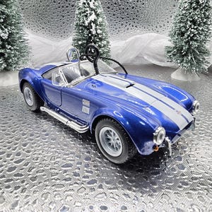 K&ouml;nnte beinhalten: Blau-wei&szlig;es Modellwagen-Ornament eines klassischen Sportwagens mit einem wei&szlig;en Streifen &uuml;ber der Motorhaube. Das Auto hat einen schwarzen Innenraum und eine schwarze Drahtschlaufe zum Aufh&auml;ngen.
