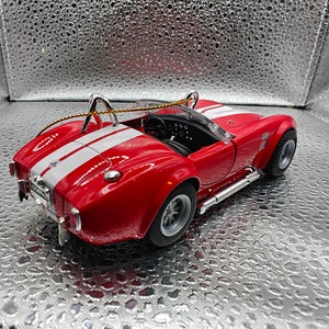 K&ouml;nnte beinhalten: Ein rotes und wei&szlig;es Spielzeugauto mit schwarzem Innenraum und silbernem Dach. Das Auto hat einen schwarzen Streifen an der Seite und einen silbernen Spoiler am Heck. Das Auto steht auf einem silbernen Hintergrund.