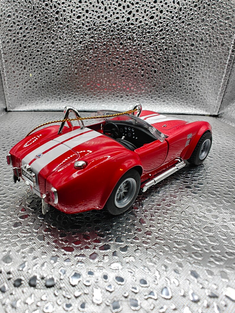 K&ouml;nnte beinhalten: Ein rotes und wei&szlig;es Spielzeugauto mit schwarzem Innenraum und silbernem Dach. Das Auto hat einen schwarzen Streifen an der Seite und einen silbernen Spoiler am Heck. Das Auto steht auf einem silbernen Hintergrund.