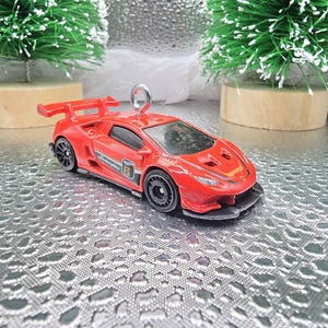 May include: Red Lamborghini race car ornament with a black spoiler and black wheels. The car has a white number "6" and the word "Lamborghini" on the side.