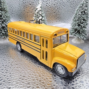 May include: A yellow toy school bus with black accents and the words "School Bus" on the side. The bus is sitting on a silver background.